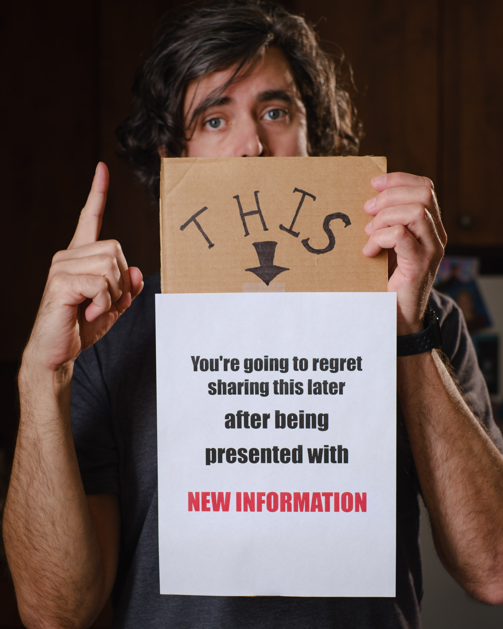 A photo of Daven holding a cardboard sign that reads "This. You're going to regret sharing this later after being presented with new information."